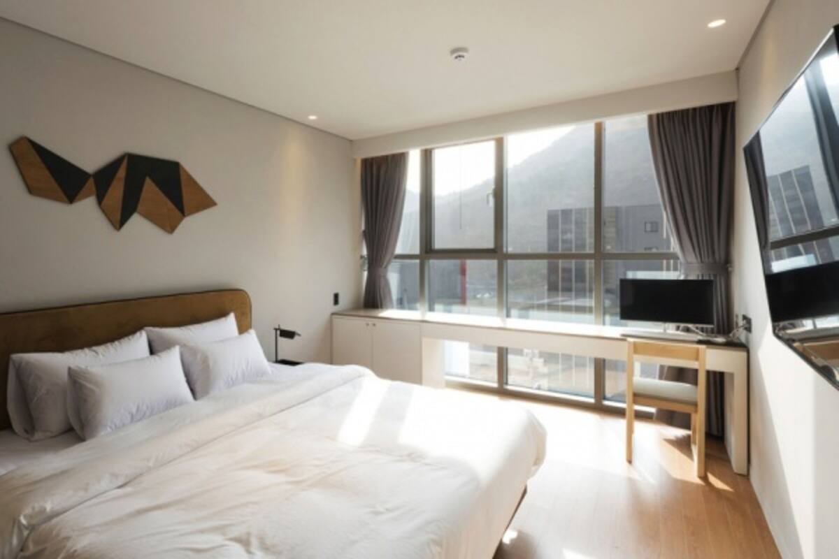 A modern hotel room with a large bed, a desk, and a large window with curtains.