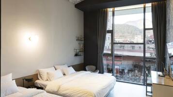 Una habitación de hotel moderna con una cama grande, un escritorio y vistas de la ciudad a través de amplias ventanas.