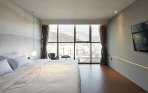 Habitación de hotel moderna con una cama grande, vistas a la ciudad a través de amplios ventanales y una pequeña zona de estar.