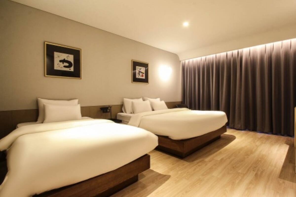 A hotel room with two beds, a wooden floor, and a large window with curtains.
