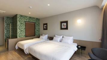 A hotel room with a large bed, a desk, and a chair. There are two beds, a window with blinds, and a wall with a green patterned design.