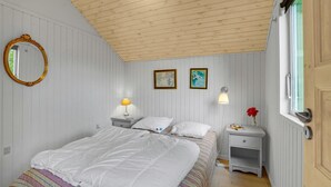 A bedroom with a wooden ceiling, a bed with white bedding, two bedside tables with lamps, a mirror, and two framed pictures on the wall.