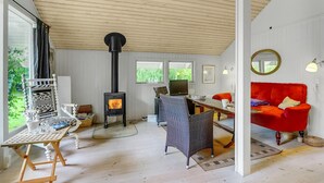 A cozy room with a wood-burning stove, wicker furniture, a red sofa, and large windows.