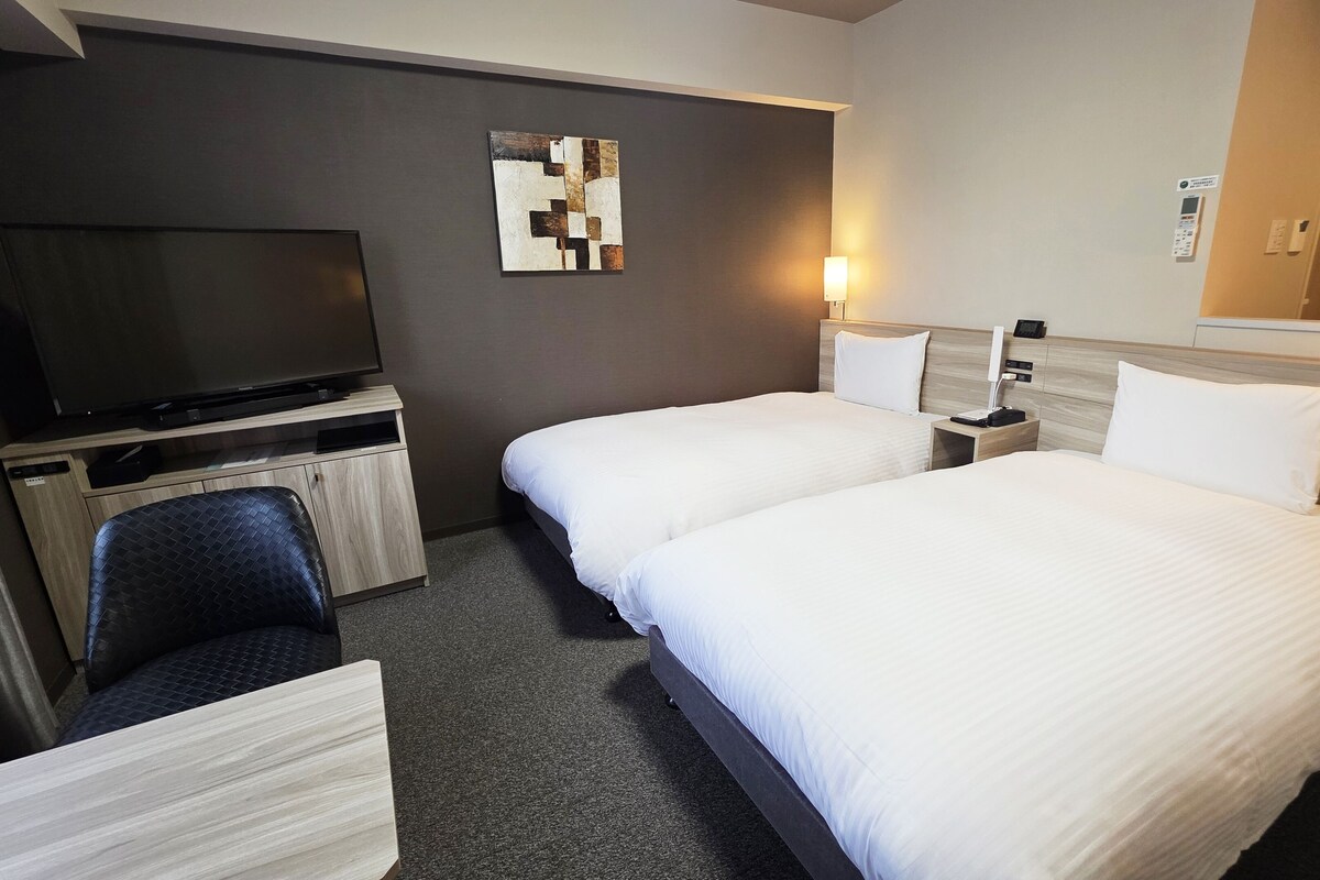 A hotel room with two beds, a TV, a desk, and a wall-mounted artwork.