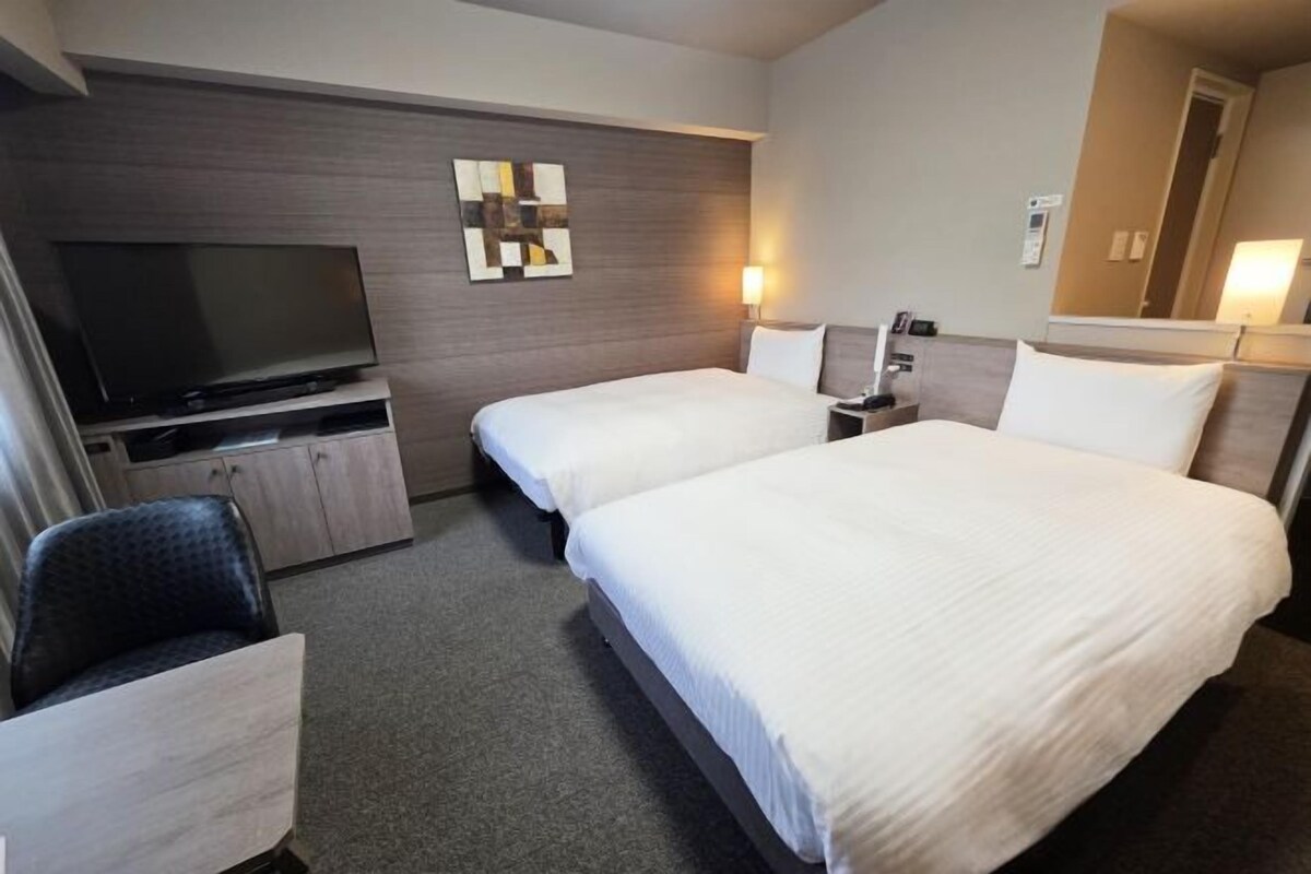 A hotel room with two beds, a TV, a desk, and a chair.