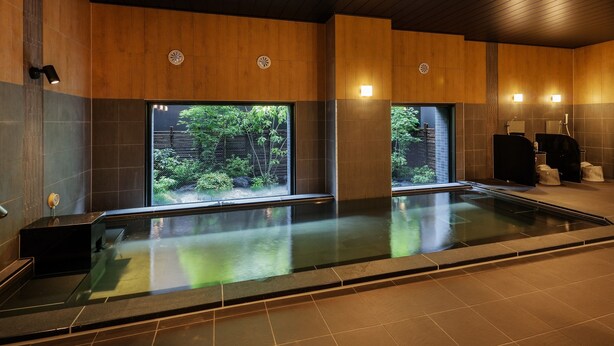 A modern spa with a large indoor pool, wooden panel walls, and natural light from windows. - Hotel Route Inn Shinano Omachi Ekimae (Omachi)