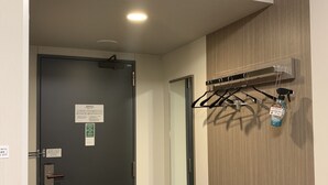 A hallway with a black door, an air conditioning unit mounted on the wall, and a coat rack with a spray bottle. - Hotel Route Inn Shinano Omachi Ekimae (Omachi)