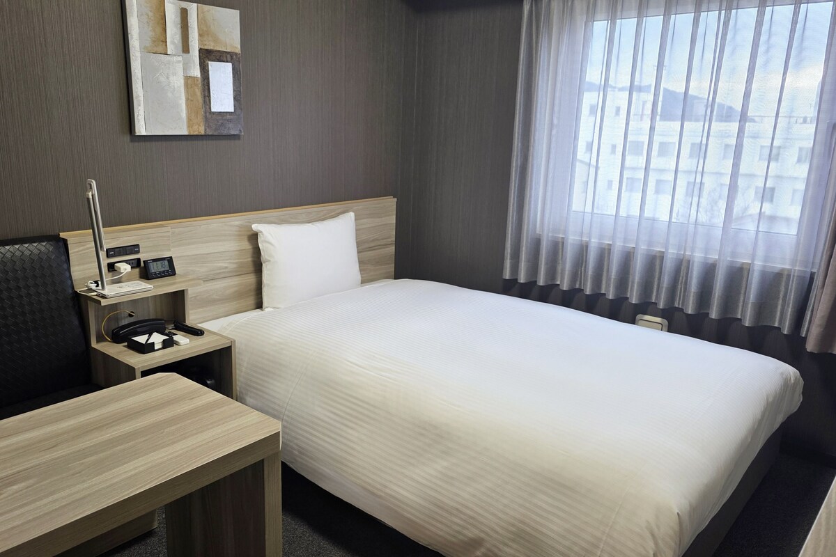 A hotel room with a bed, bedside table, lamp, and a mirror on the wall.