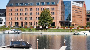 A hotel with a brick facade, a large tree in front, and a modern glass building to the right. - Hotel Hafenspeicher - 14023 - Classic (Leer (Ostfriesland))