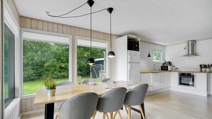 A modern kitchen with a wooden table, grey chairs, and a view of the garden through large windows. - 3 bedroom amazing home in Hemmet (Hemmet)