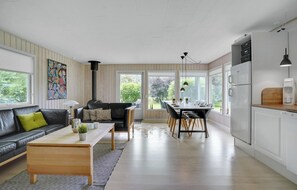 A modern kitchen with a dining area, wooden flooring, and large windows offering a view of the outdoors.