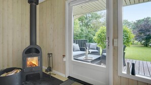 A room with a wood-burning stove, a door leading to an outdoor patio with a table and chairs, and a view of a garden. - 3 bedroom amazing home in Hemmet (Hemmet)