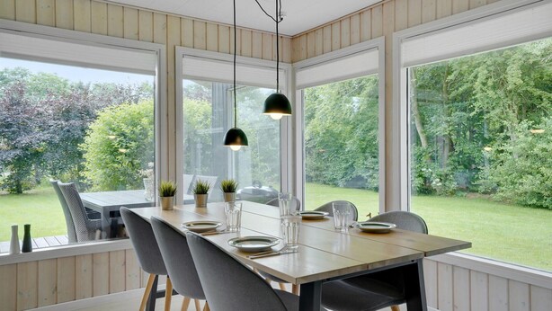 A dining area with a table set for four, large windows, and a view of a garden. - 3 bedroom amazing home in Hemmet (Hemmet)