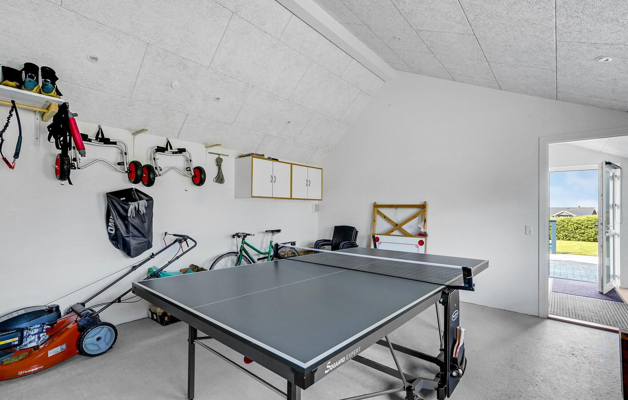 A room with a ping pong table, a bicycle, and a lawnmower.