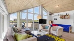 A modern living room with a large window, a flat-screen TV, and a blue sofa. - Cozy home in Vinderup with sauna (Vinderup)