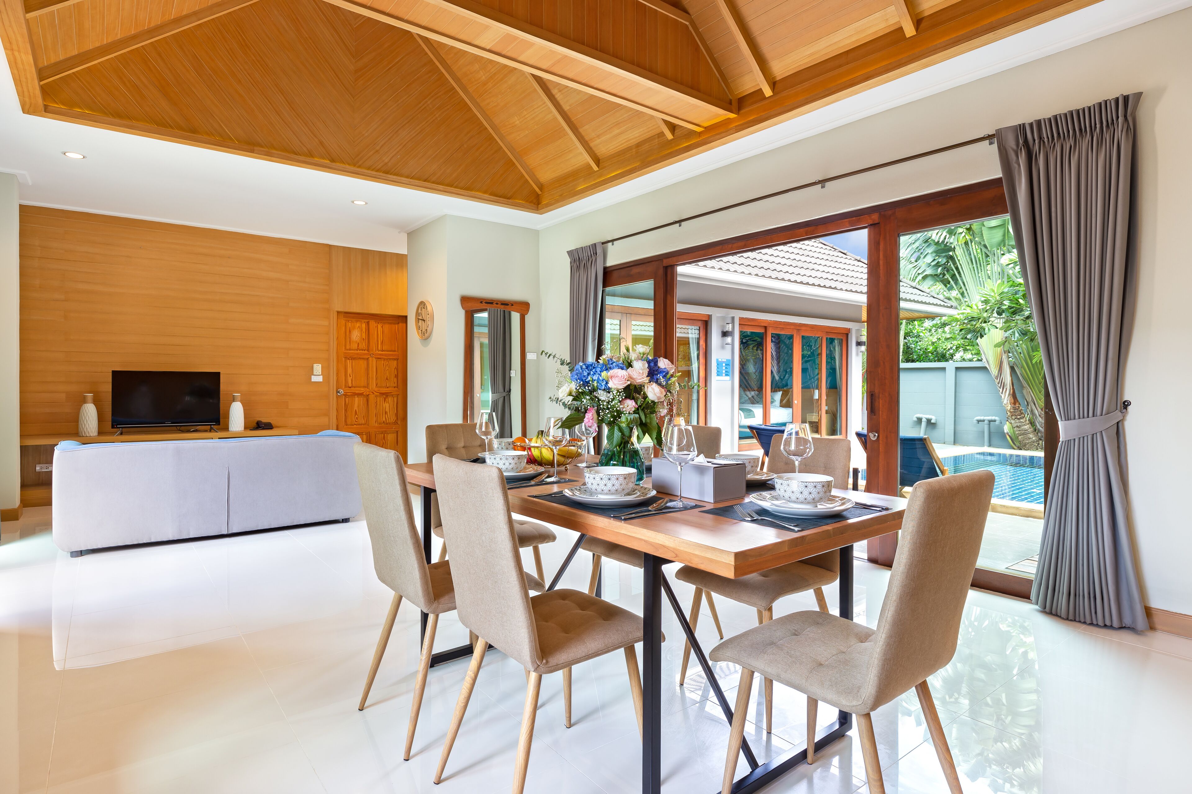 Un espace repas moderne avec une table en bois, des chaises de couleur beige et une grande fenêtre donnant sur une piscine.