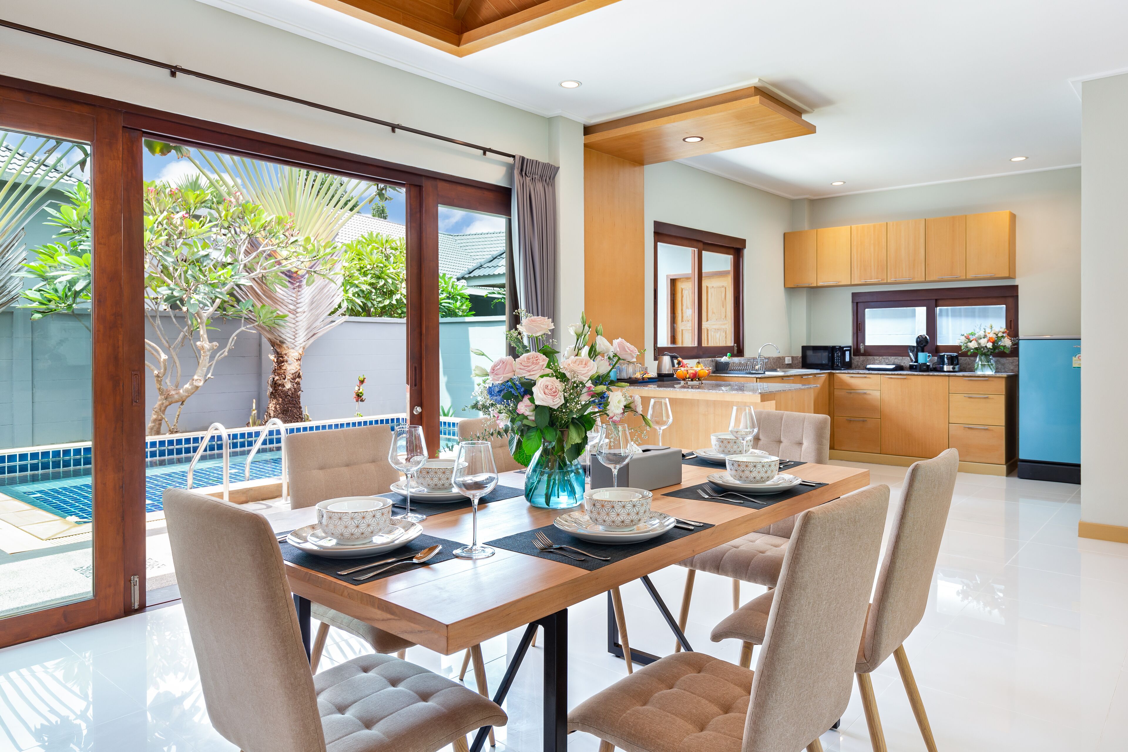 Un'elegante zona pranzo con un tavolo di legno apparecchiato per quattro persone, circondata da sedie. Un'ampia finestra si affaccia su una piscina e sul verde.