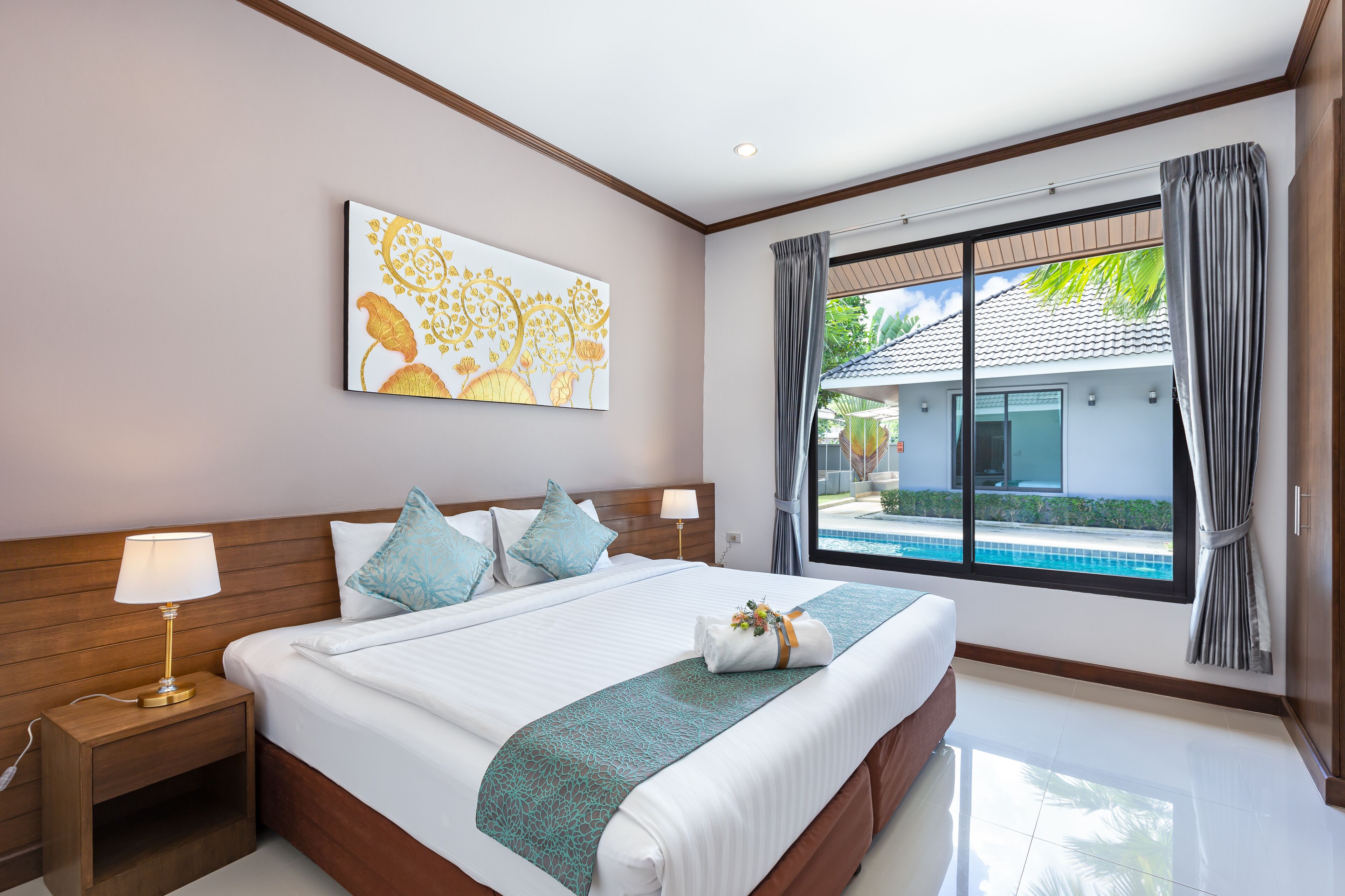 A hotel room with a large bed, a nightstand, a window with a view of a swimming pool, and a painting on the wall.