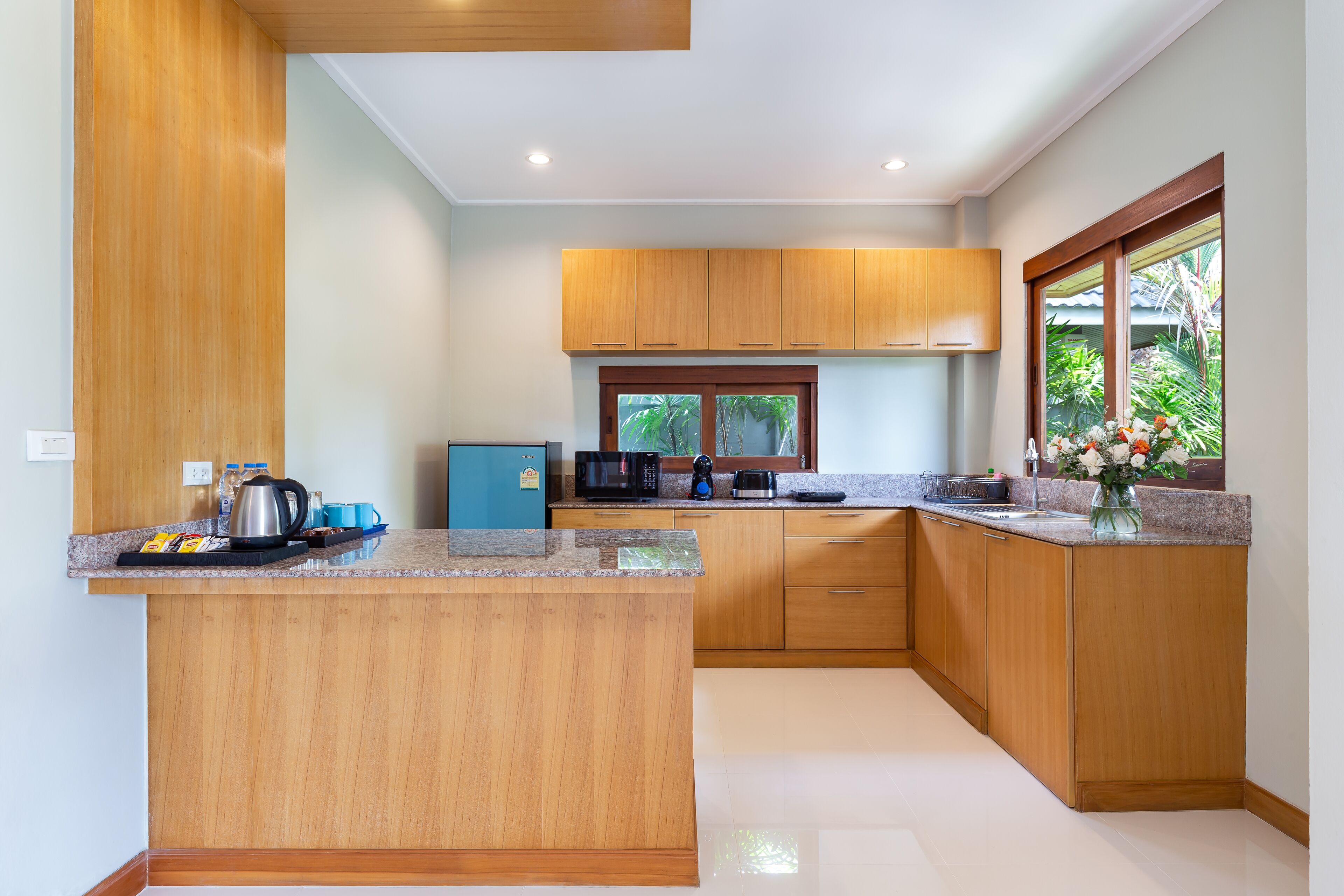 A modern kitchen with wooden cabinets, a granite countertop, and a window with a view of greenery.