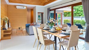 A modern dining area with a wooden ceiling, a glass table, and beige upholstered chairs. - Lady Naya Villas (Rawai)