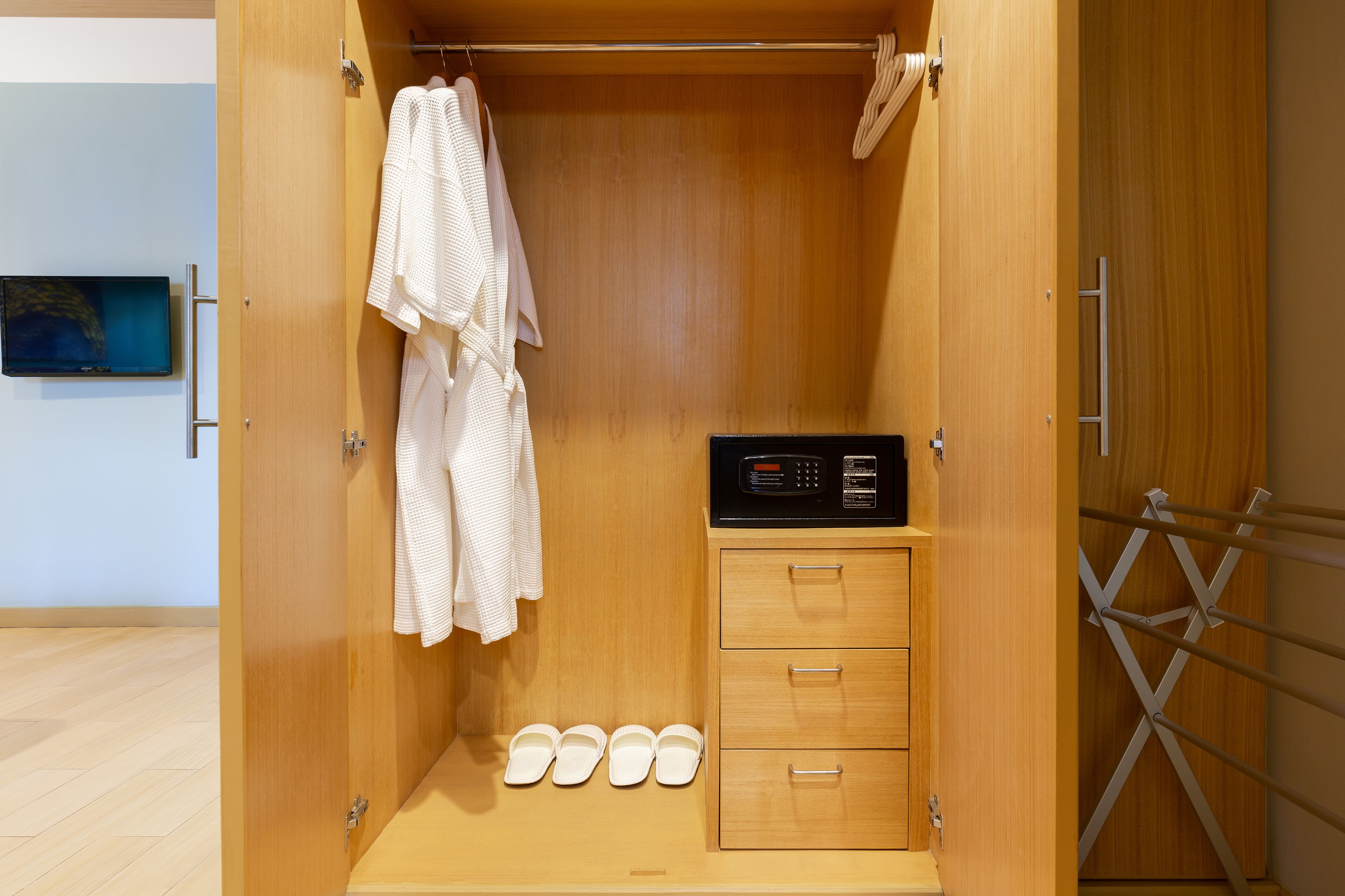 A wooden walk-in closet with a microwave, a hanging rack, and a pair of slippers.