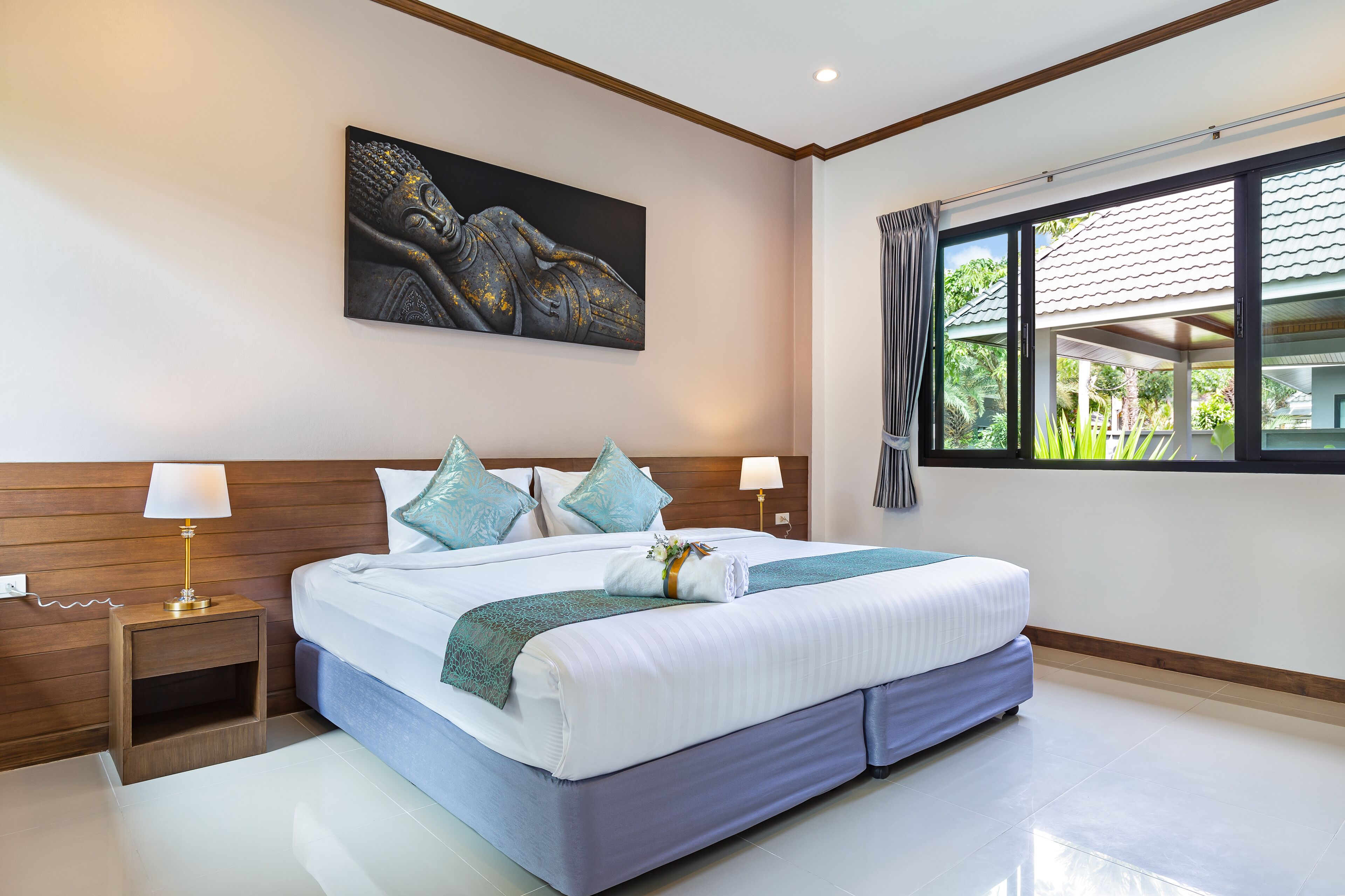 Una habitación de hotel moderna con una cama grande, cabecera de madera, un cuadro sobre la cama y una ventana con vistas a zonas verdes.