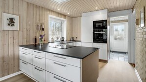 Une cuisine moderne dotée d’un îlot central, de meubles blancs et d’un plan de travail noir. Une fenêtre laisse entrer la lumière naturelle et offre une vue sur les arbres à l’extérieur.