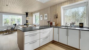 Une cuisine moderne avec des meubles blancs, un plan de travail noir et une grande fenêtre donnant sur la forêt.