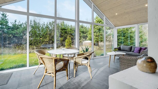 Un espace intérieur vaste et lumineux, doté de grandes fenêtres, de meubles en osier et offrant une vue sur un jardin.
