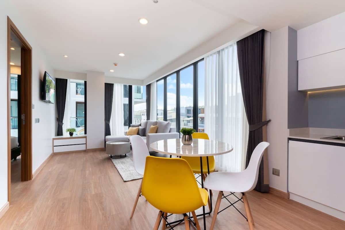 Una sala de estar moderna con una mesa de comedor redonda, sillas amarillas, un sofá y un televisor montado en la pared.