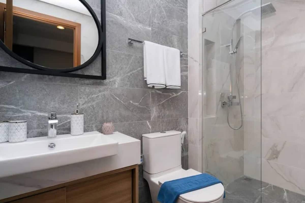 Un baño moderno con salpicadero de mármol, un lavabo blanco, un inodoro y ducha con mampara de cristal.
