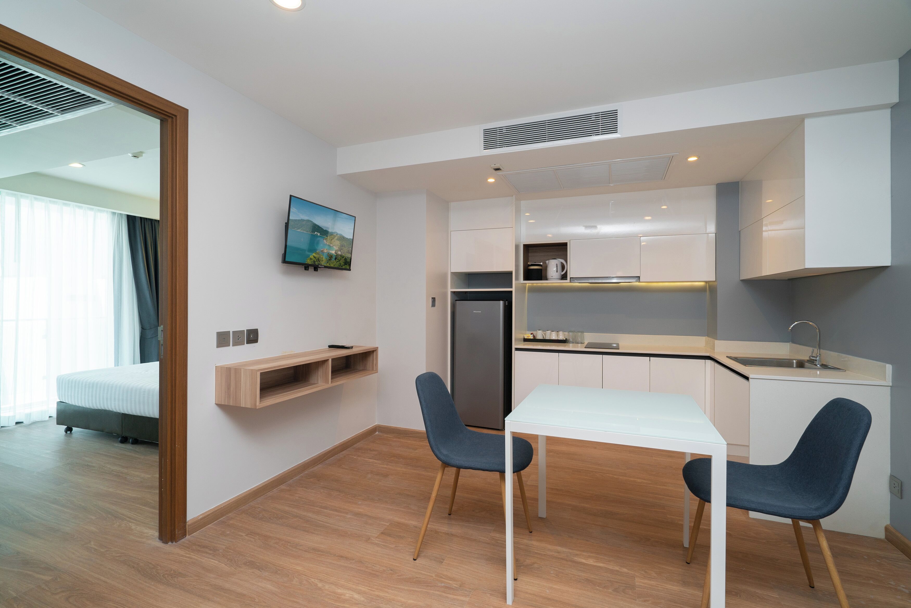 Habitación de hotel pequeña con kitchenette, una zona de comedor con dos sillas, una cama y un televisor montado en la pared.