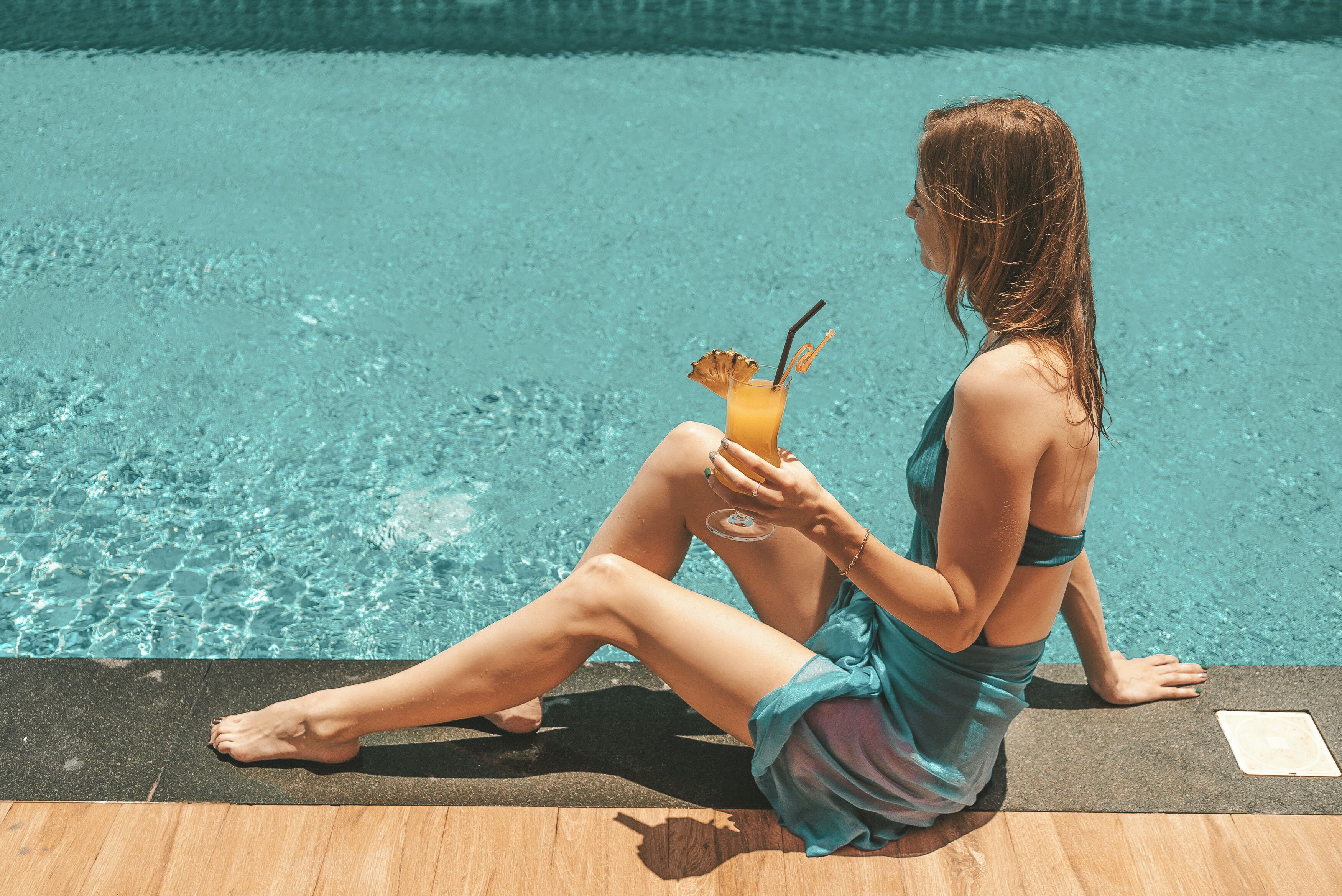 A person sitting by a pool with a drink.