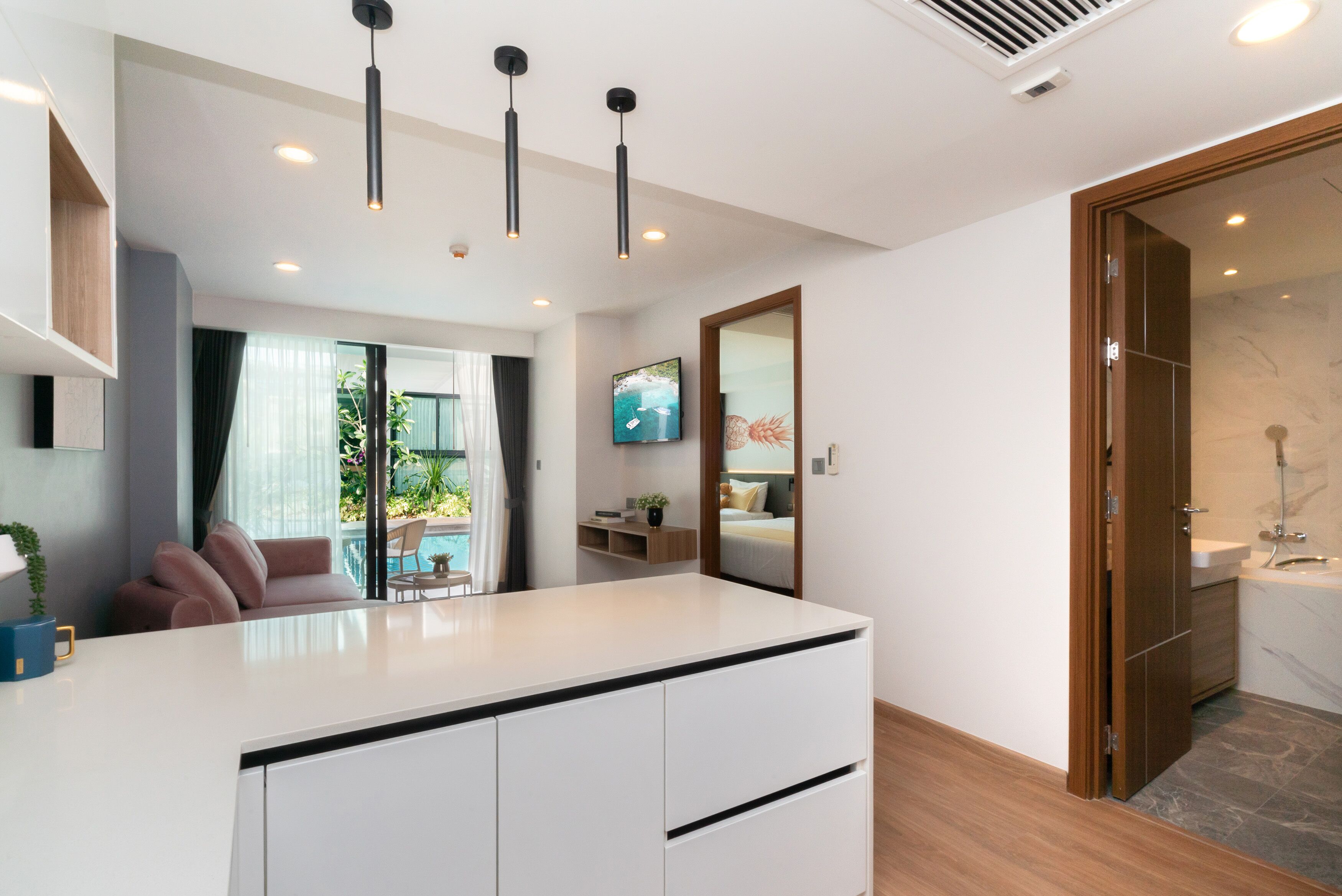 A modern hotel room with a central island, a large mirror, a TV, and a view of the pool area.