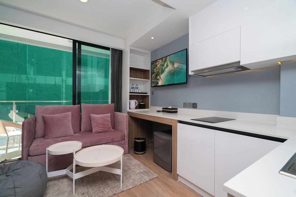 Un espacio habitable moderno y funcional con sofá, una mesita, zona de cocina con lavavajillas y un amplio ventanal con vistas a un balcón.
