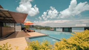 Una piscina con sillas de descanso y una sombrilla, rodeada de vegetación y un edificio moderno.