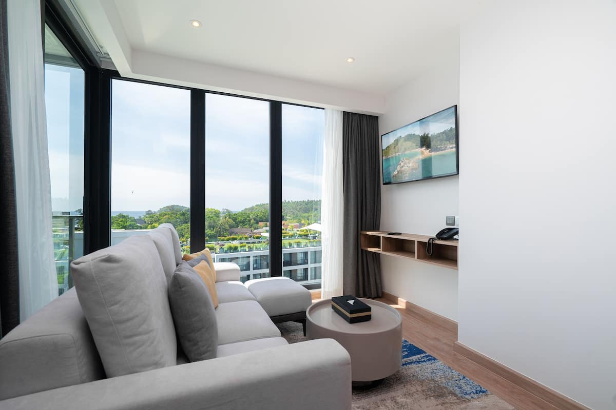 Una sala de estar moderna con un sofá grande, una mesa de centro redonda y vistas a un paisaje urbano a través de amplios ventanales.