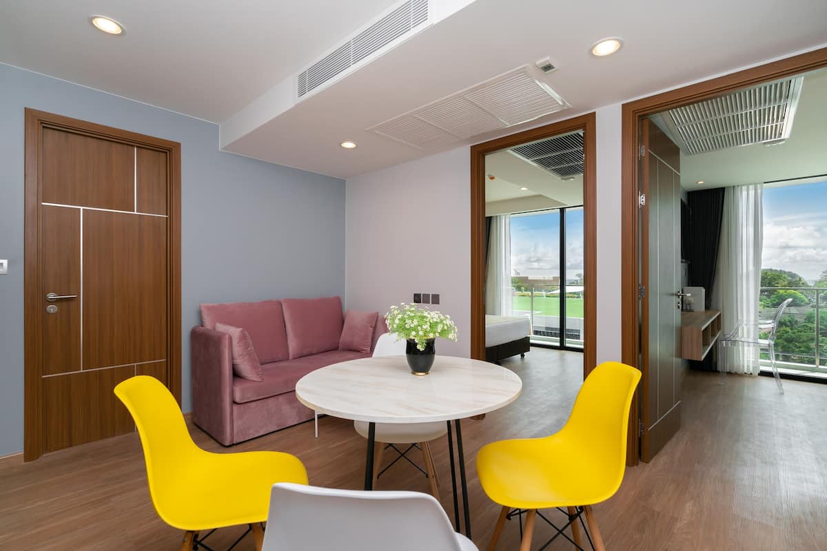 Una sala moderna con una mesa redonda, dos sillas amarillas, un sofá rosa y una puerta de madera.