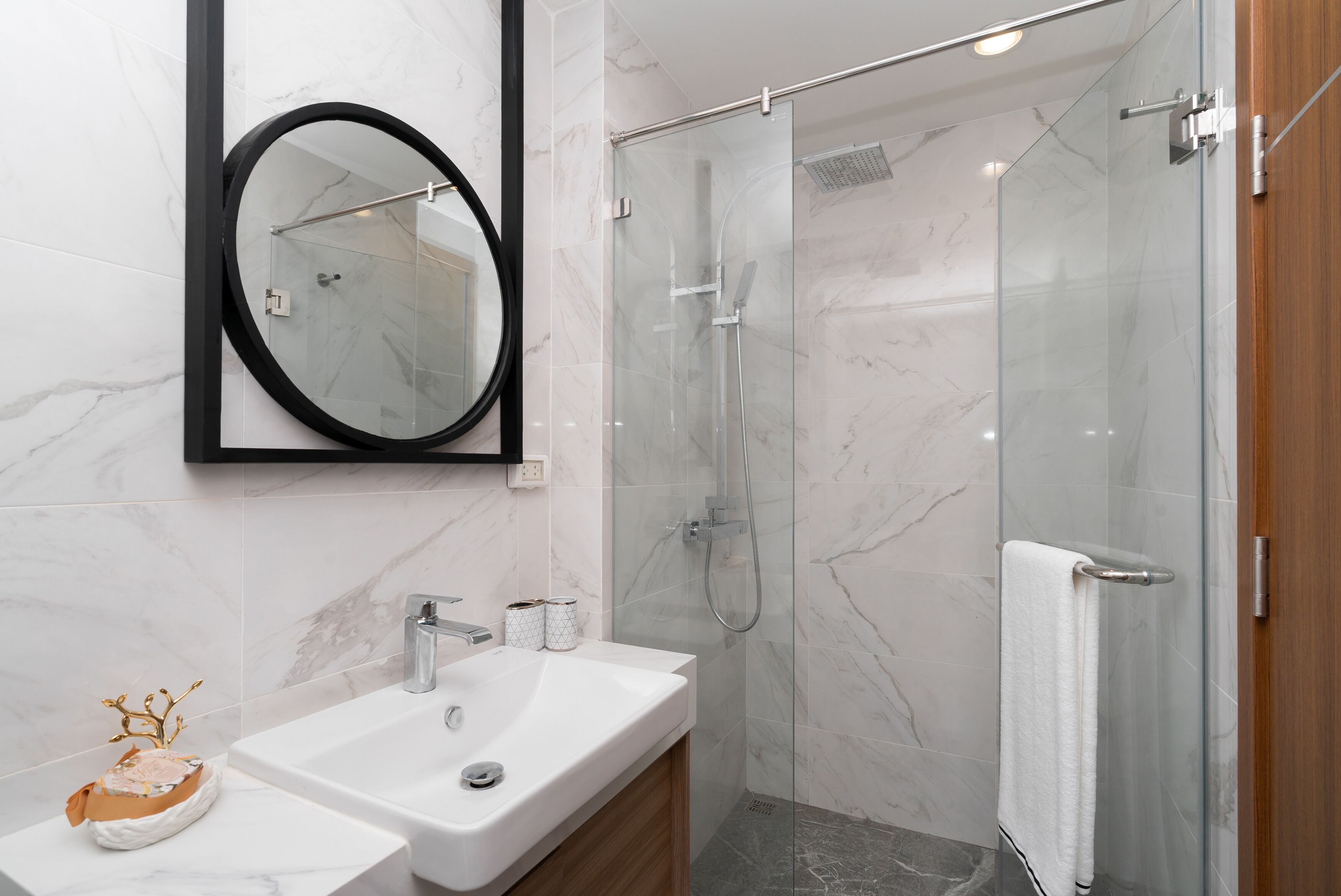 Un bagno moderno con doccia vetrata, lavandino bianco e specchio tondo.
