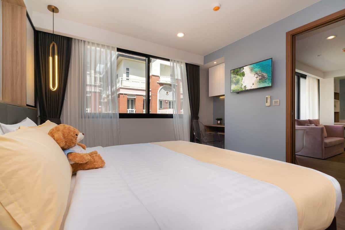 Habitación de hotel con una cama grande, un escritorio, una silla, un televisor y vistas a edificios a través de la ventana.