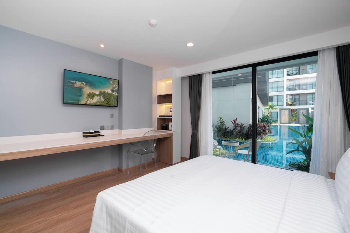 Una habitación de hotel moderna con una cama grande, un escritorio, una silla, un televisor montado en la pared y un balcón con vista a la piscina.