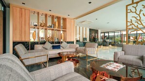 Una sala de estar moderna con un sofá, sillones y una mesa de centro. Se ve un aparador de madera con objetos decorativos y un ventanal grande al fondo.