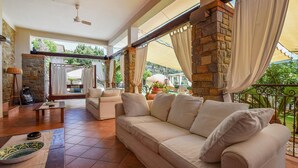 A spacious living area with a beige sofa, a coffee table, and a stone fireplace. There is a balcony with a view of greenery. - Nice home in Laureana Cilento (Laureana Cilento)