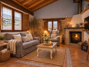A cozy living room with a stone fireplace, a sofa, a chair, and a television. - Romantic Getaway in Asturias · Hot Tub, Fireplace, and Views (Santa Maria - Proaza)