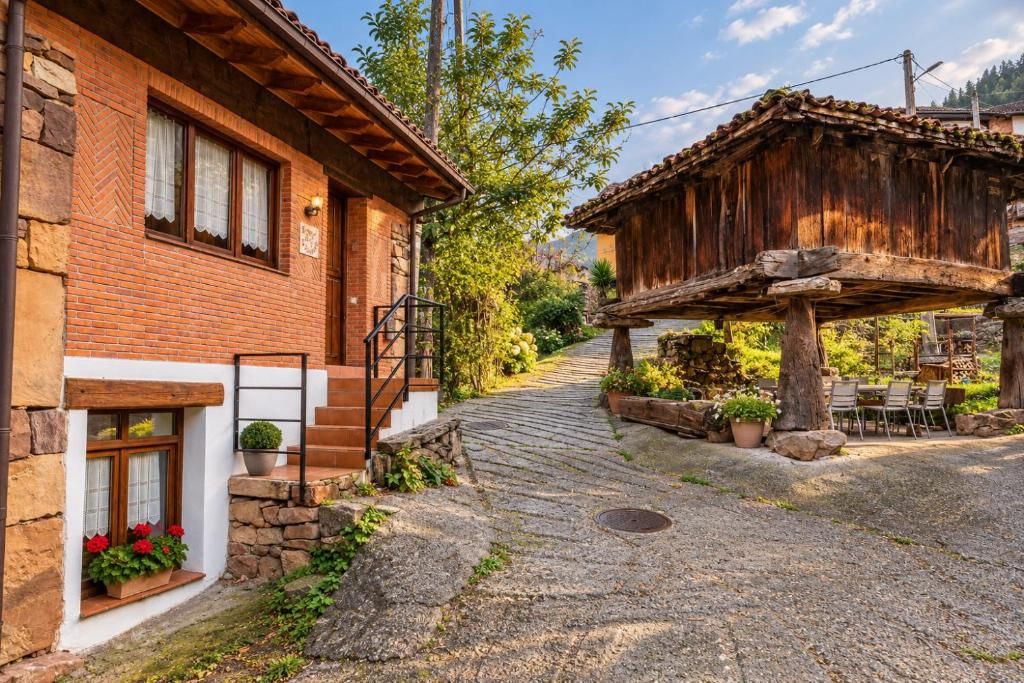 Edifici rústic amb façana de pedra, estructura de fusta i teulada inclinada, i un camí empedrat que condueix a una zona de seients.