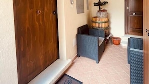A wooden door with a welcome mat, a small seating area with wicker furniture, and a barrel in the background. - Da Nonna Pasqualina (Ciorlano)