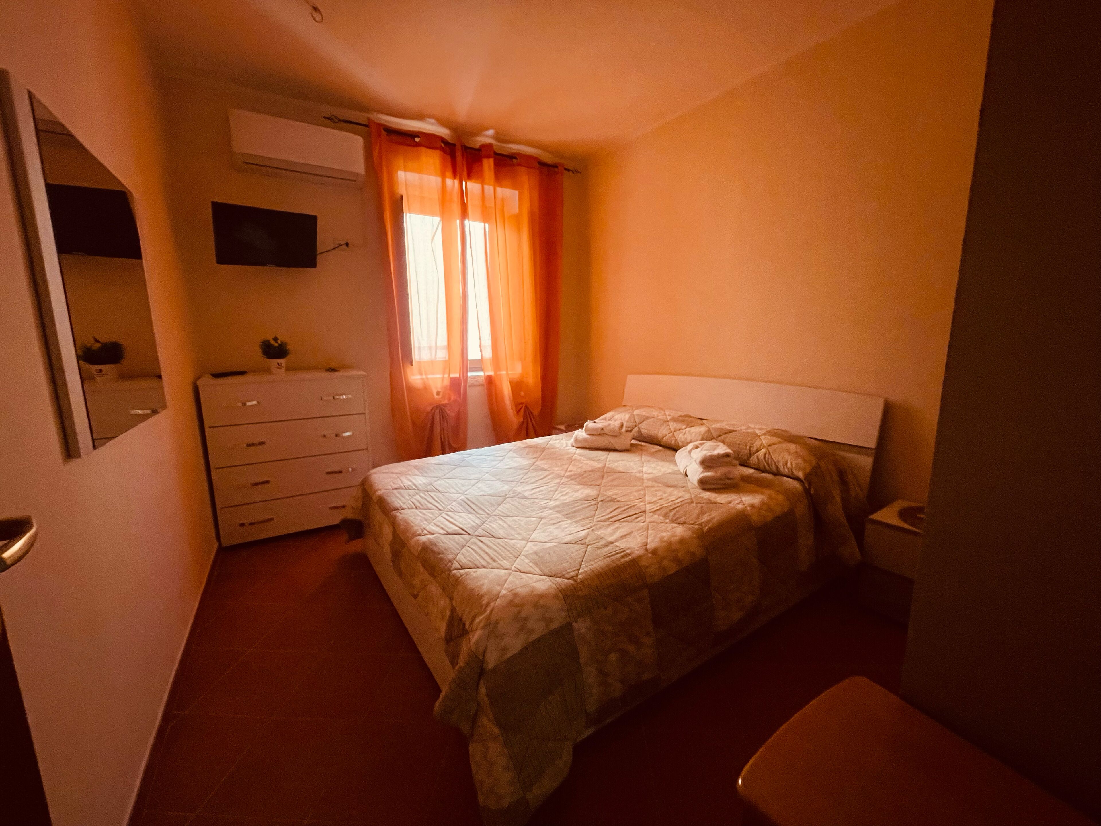 Un dormitorio con una cama, un aparador, un espejo y un televisor en la pared.