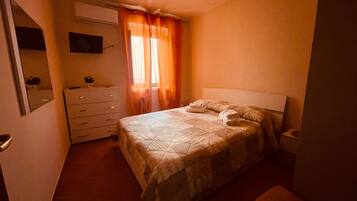 Un dormitorio con una cama, un aparador, un espejo y un televisor en la pared.