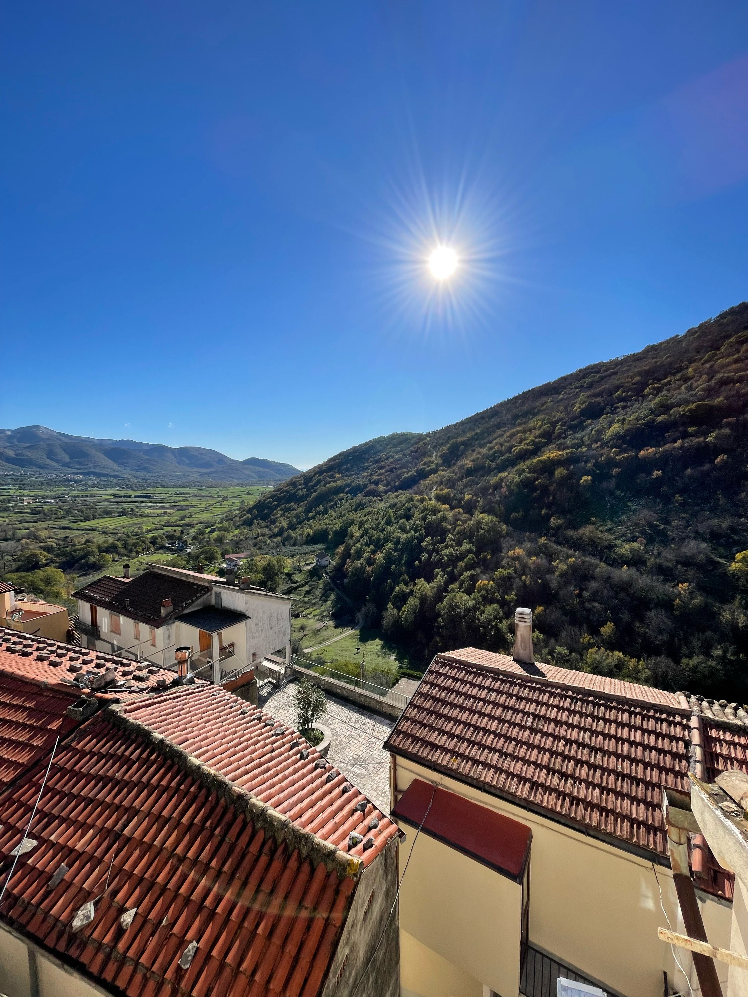 A view of terracotta-roofed buildings with a valley and mountains in the background.
