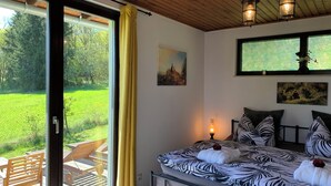 A bedroom with a bed, a painting, a window, and a view of a green field.